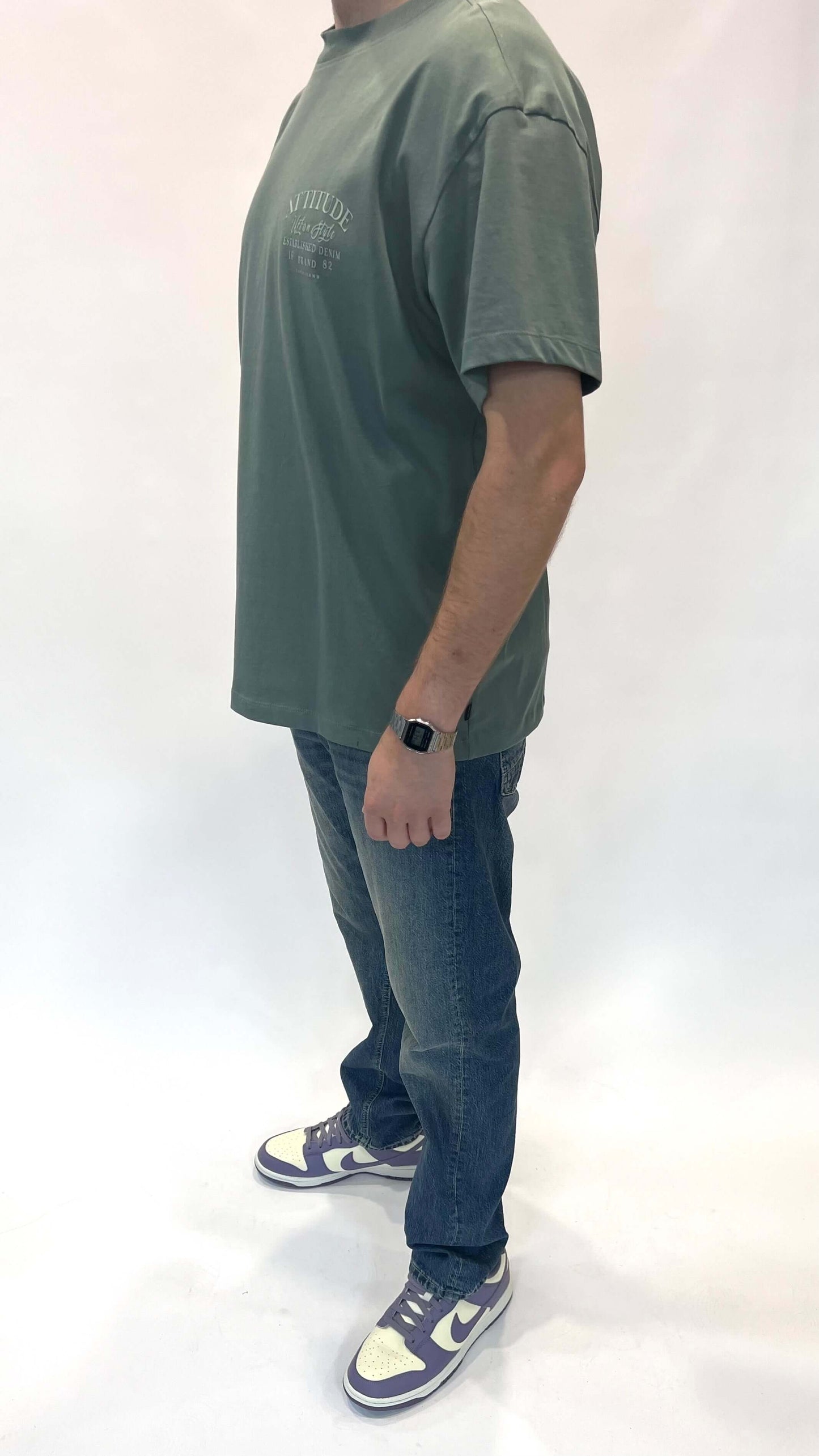 Man in een losse groene t-shirt en spijkerbroek, stijlvol en comfortabel voor dagelijks gebruik.