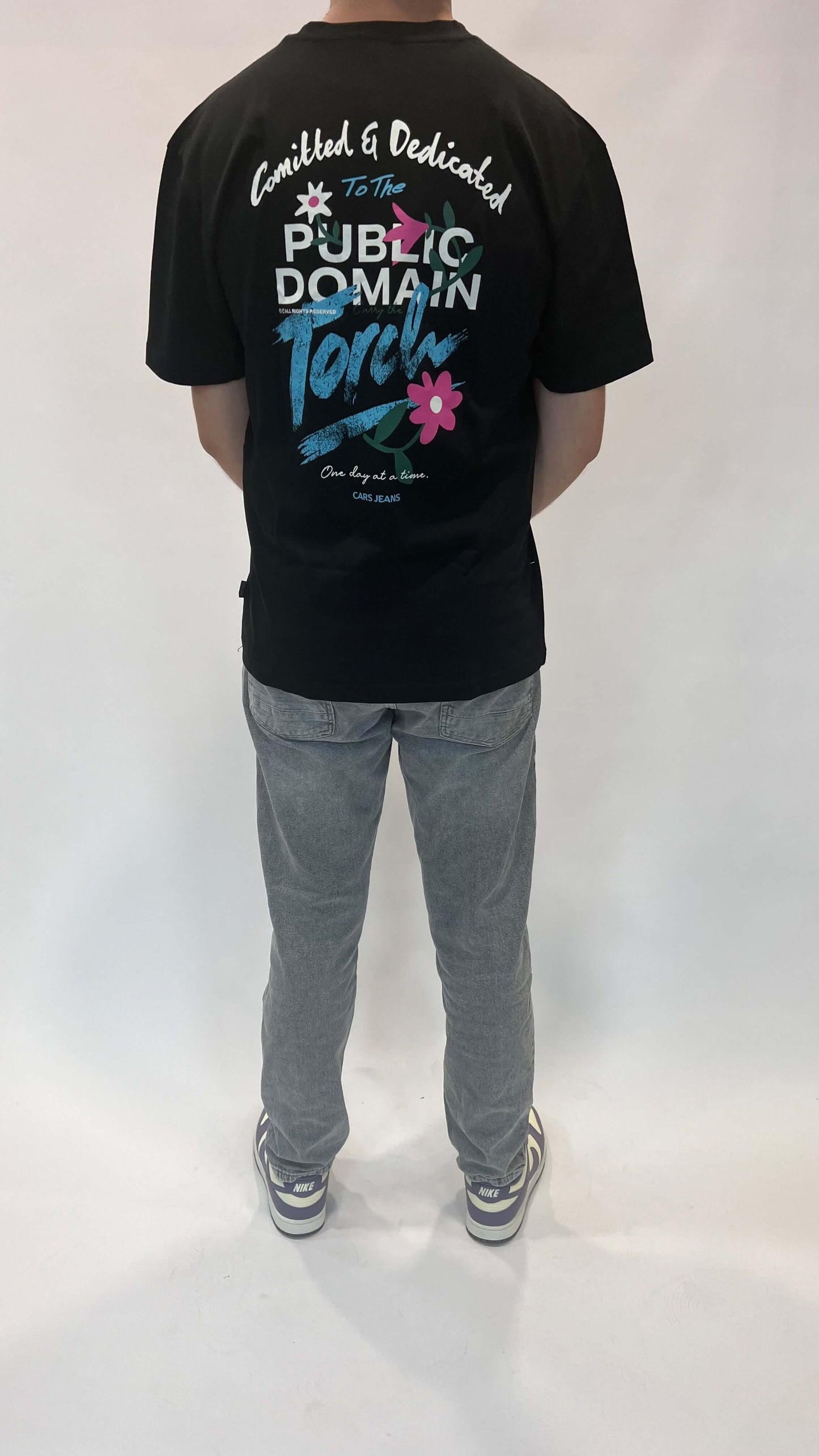 Zwarte t-shirt met tekst en grafische print, gedragen door een persoon van achteren.