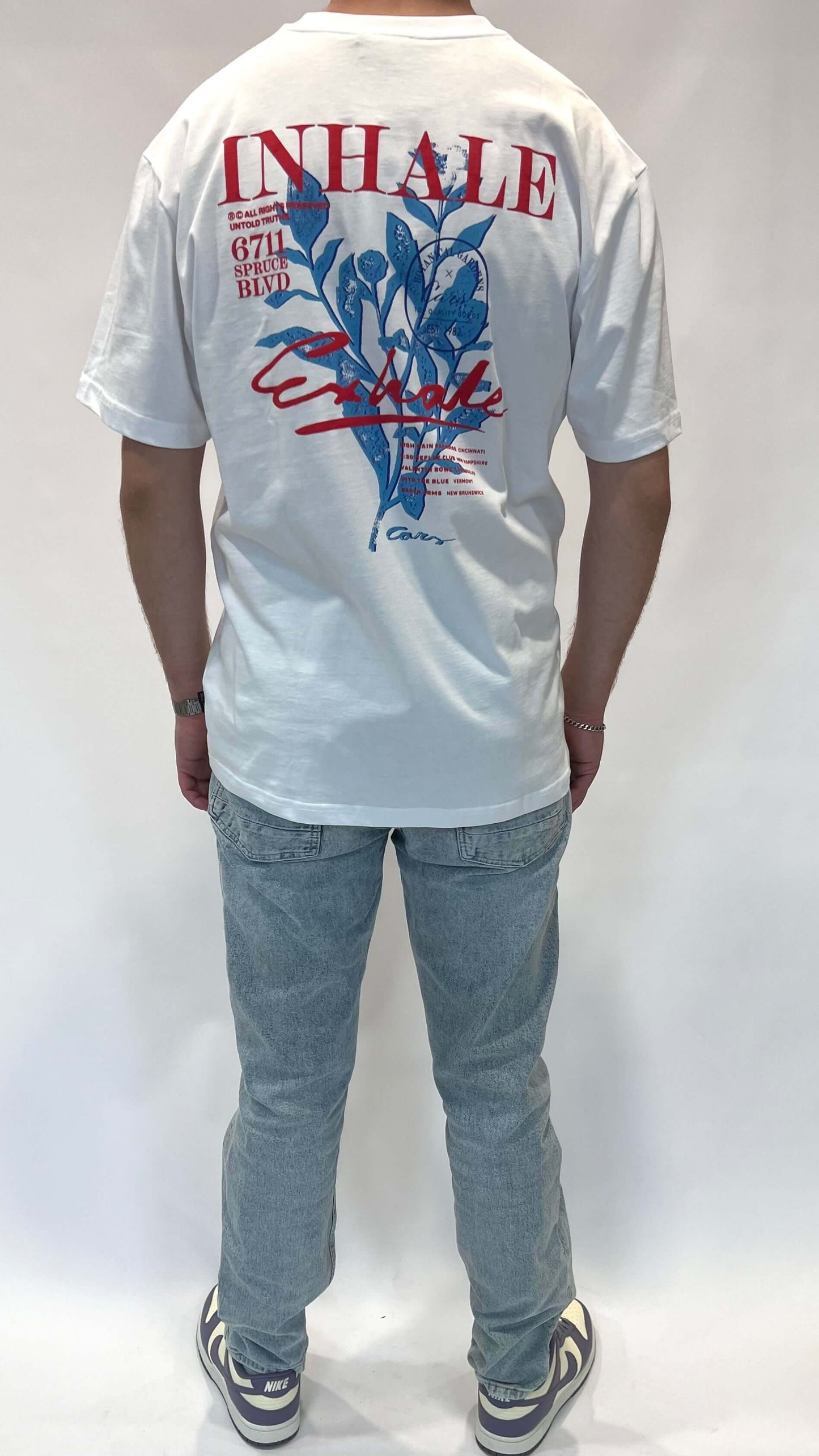 Model in een wit t-shirt met de tekst 'INHALE' en een grafisch ontwerp op de achterkant.