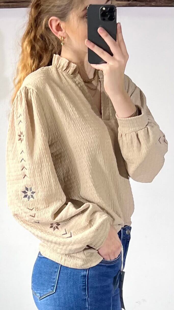 Beige blouse Milou met broderie details, model poseert met smartphone voor spiegel.