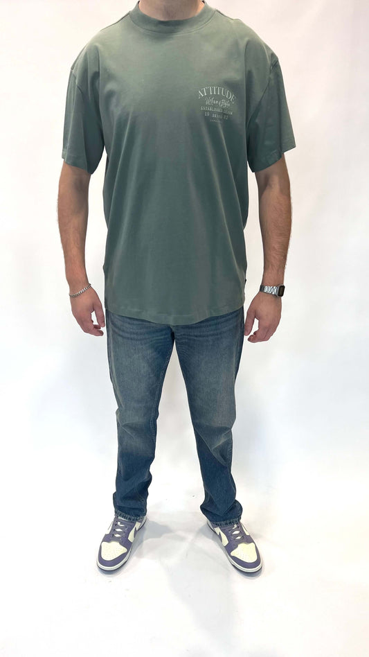 Man in groene t-shirt en spijkerbroek, casual outfit met sneakers en accessoires.